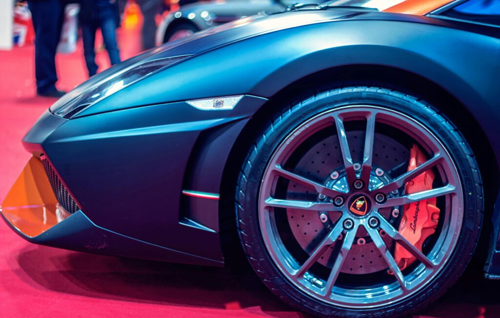 Detailed view of a luxury sports car wheel on a red carpet at an auto show.
