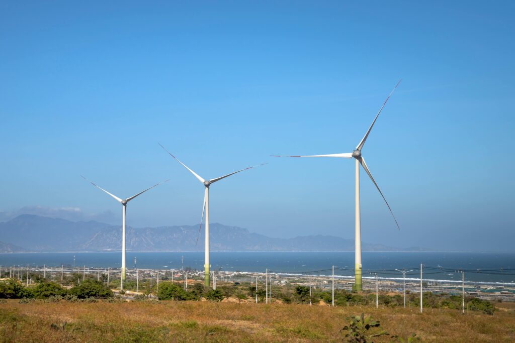 Rows of wind generators on land with plants against sea and mountain in daylight